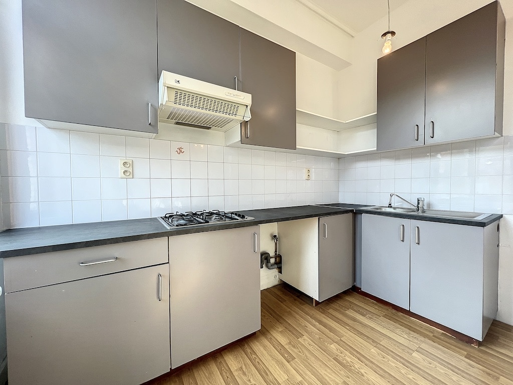Cuisine moderne minimaliste avec meubles gris laqués, comptoirs sombres et sol en bois chaleureux.
