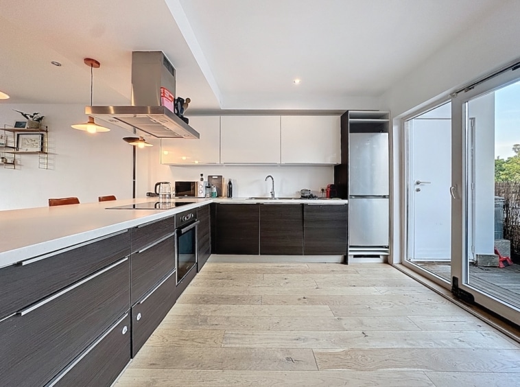 Cuisine moderne lumineuse avec meubles en bois foncé, éclairage élégant et accès extérieur en verre.