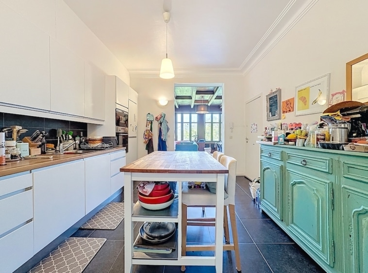 Cuisine moderne lumineuse avec îlot en bois, meubles blancs et cabinet vert menthe.