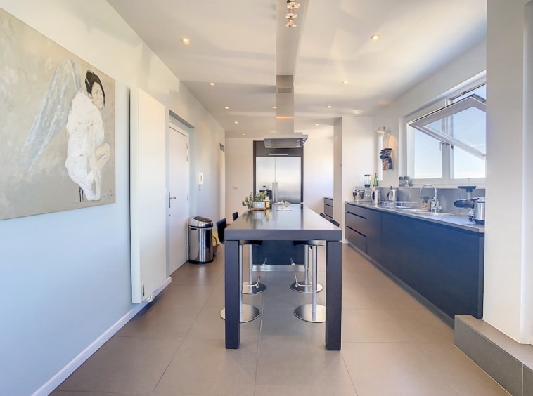 Cuisine contemporaine lumineuse avec îlot central, meubles sombres et grandes fenêtres naturelles.
