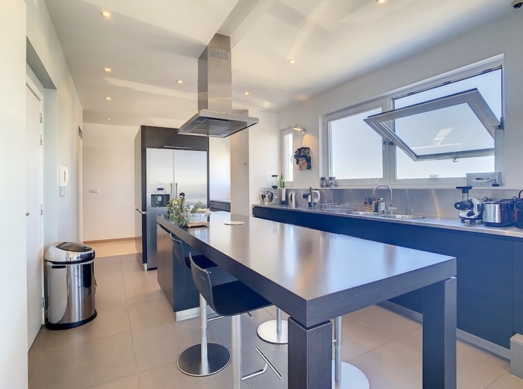 Cuisine moderne avec îlot central, grands fenêtres, meubles foncés et appareils en inox élégants.