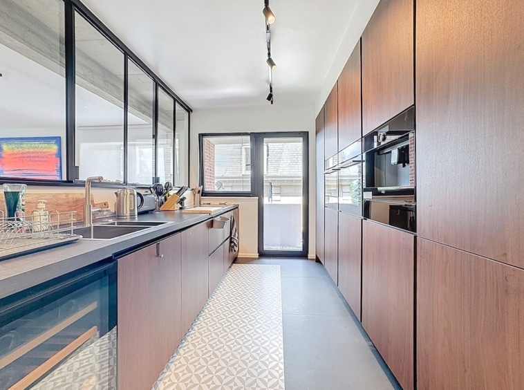 Cuisine contemporaine lumineuse avec meubles en bois, plan noir, appareils intégrés et décor géométrique.