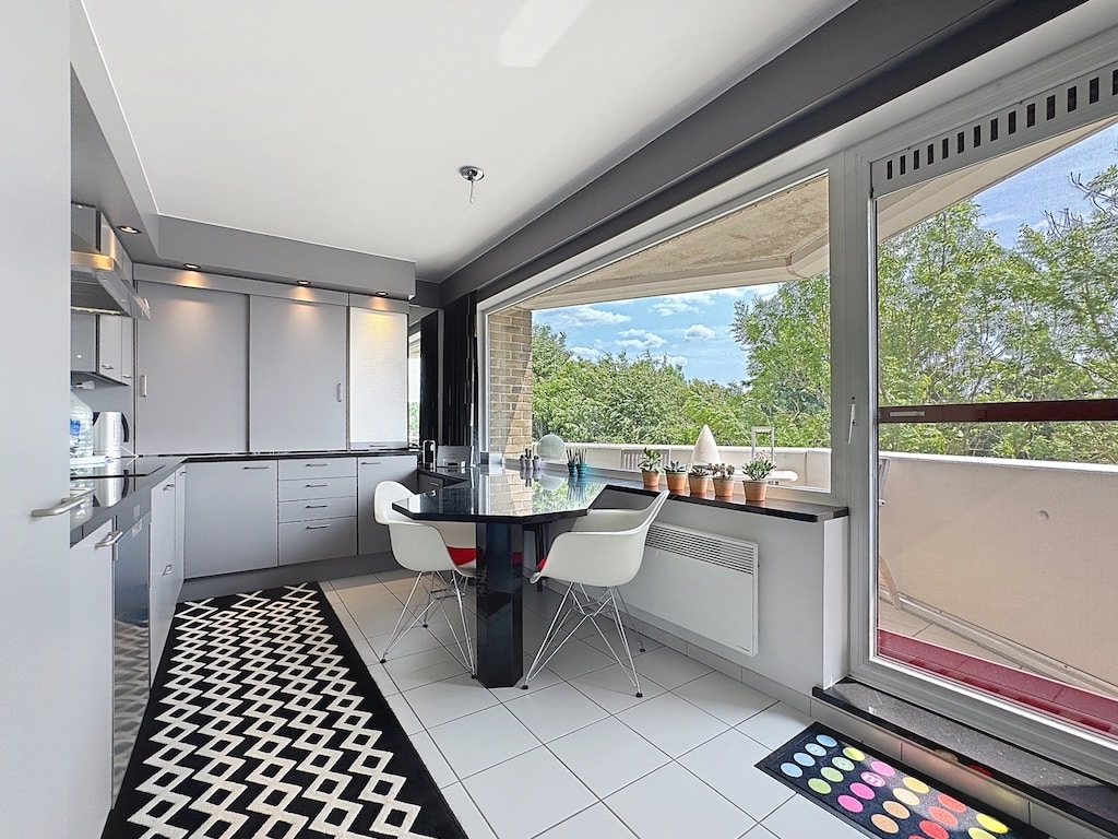 Cuisine moderne lumineuse avec vue, mobilier gris et blanc, tapis géométrique et plantes vertes.