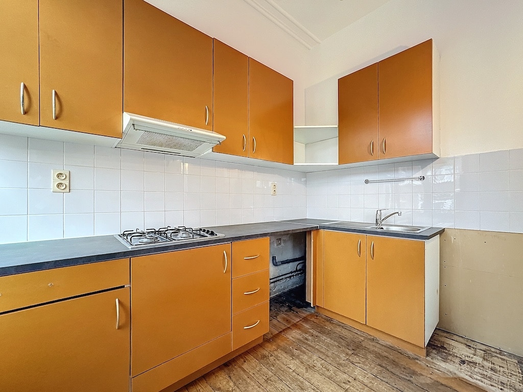 Cuisine chaleureuse avec mobilier en bois, plaque gaz, évier inox et sol en bois naturel.