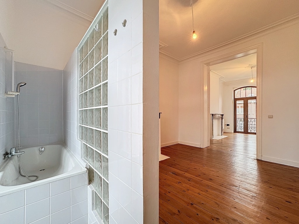 Intérieur lumineux avec baignoire moderne, parquet en bois, arches élégantes et ambiance chaleureuse.