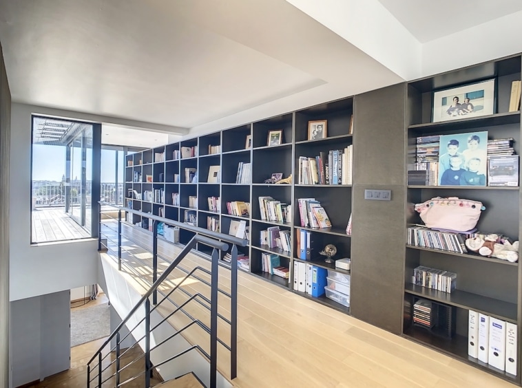 Espace moderne avec bibliothèque, escalier en bois et lumière naturelle immersive.