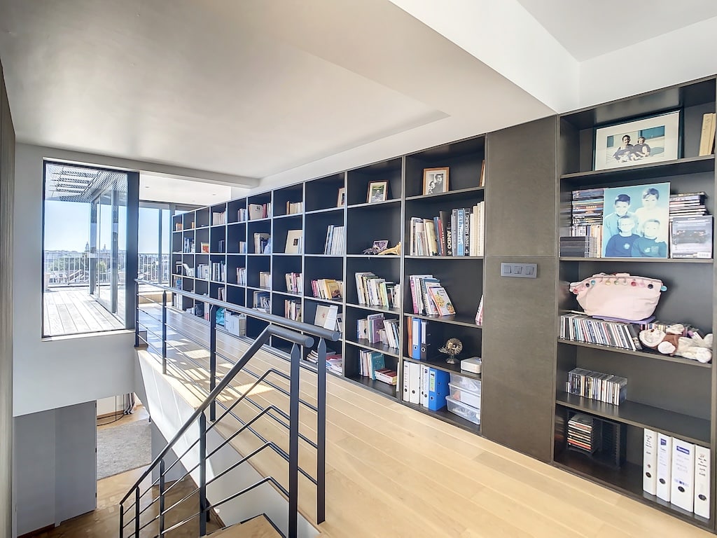 Espace moderne avec bibliothèque, escalier en bois et lumière naturelle immersive.