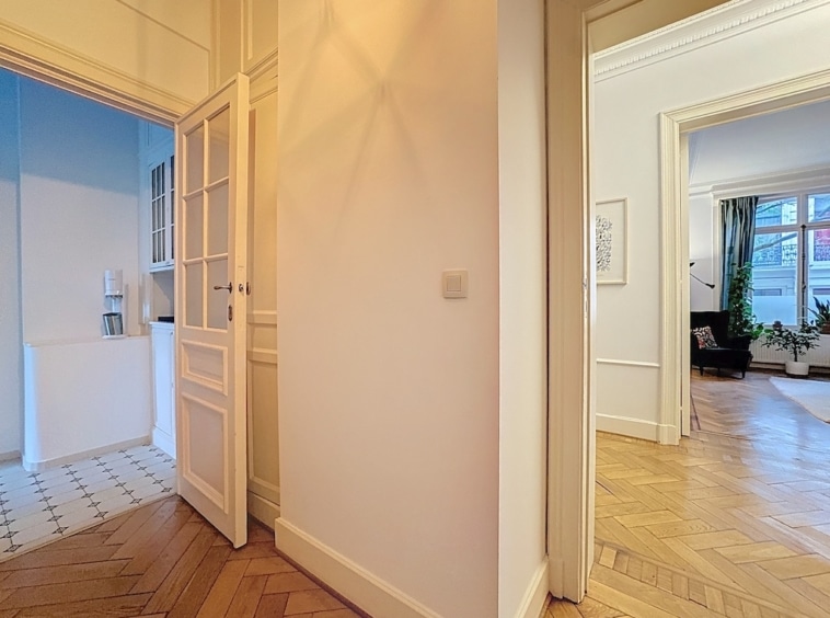 Hall lumineux avec parquet chevrons, cuisine moderne et salon cosy avec plantes et lumière naturelle.