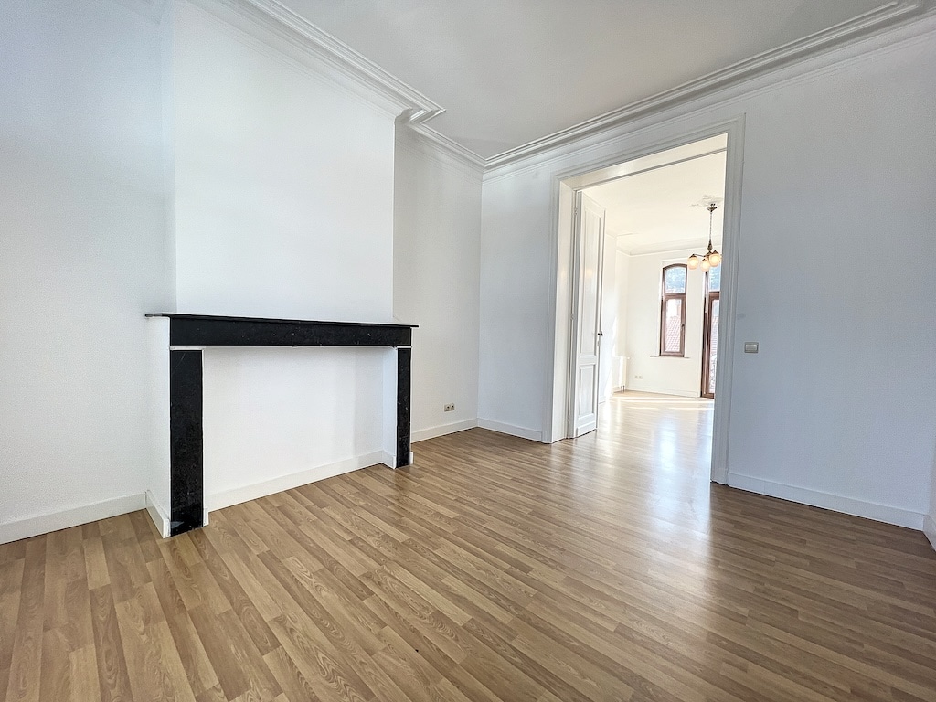 Intérieur lumineux avec sol en bois clair, murs blancs et cheminée en marbre noir moderne.