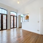 Salon lumineux avec parquet en bois, grandes fenêtres et accès à terrasse, style moderne et classique.