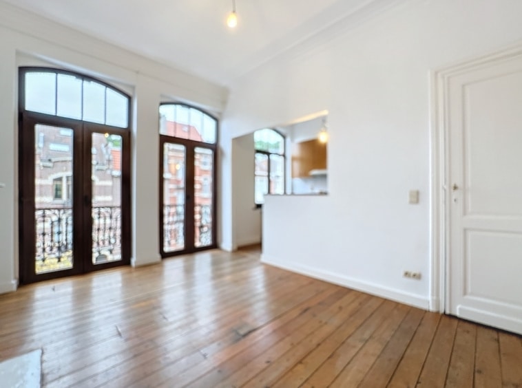 Salon lumineux avec parquet en bois, grandes fenêtres et accès à terrasse, style moderne et classique.