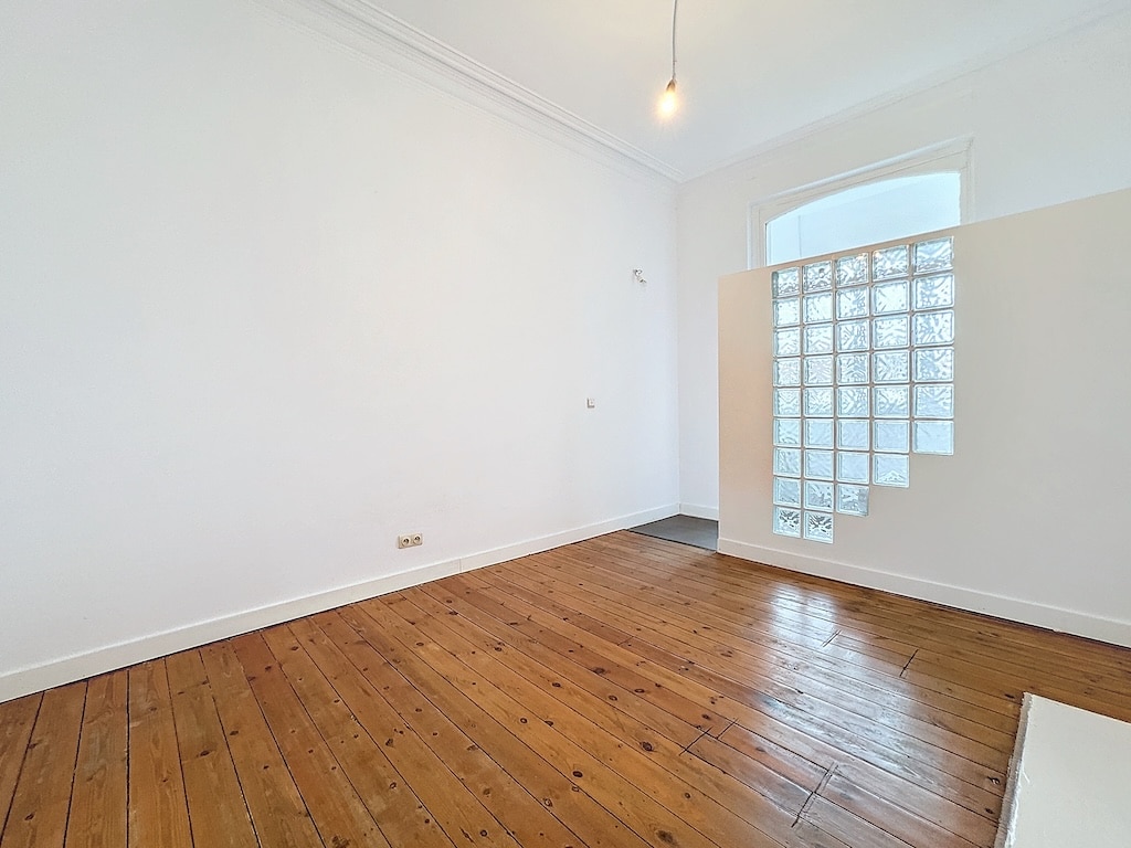 Espace minimaliste moderne avec murs blancs, sol en bois, lampe suspendue et mur en verre.