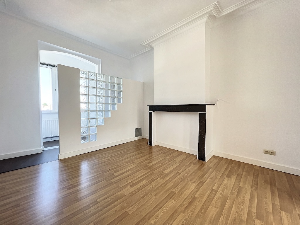 Espace contemporain lumineux avec mur en blocs de verre, sol en bois et cheminée noire élégante.