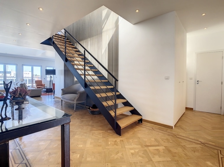 Escalier moderne en bois avec balcon en métal noir dans un intérieur lumineux et épuré.
