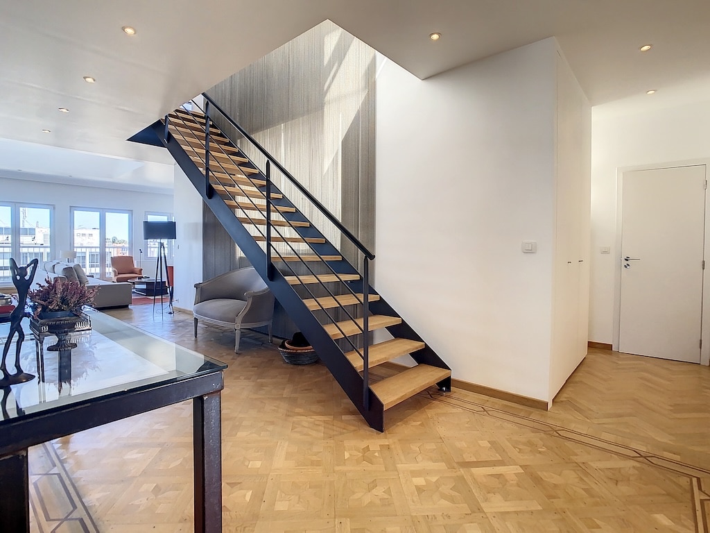 Escalier moderne en bois avec balcon en métal noir dans un intérieur lumineux et épuré.