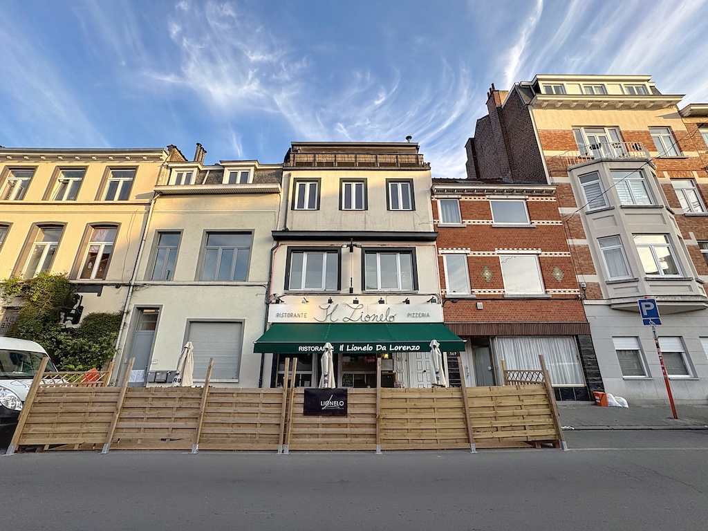 Rue colorée avec café convivial, bâtiments en briques, ambiance chaleureuse sous ciel bleu.