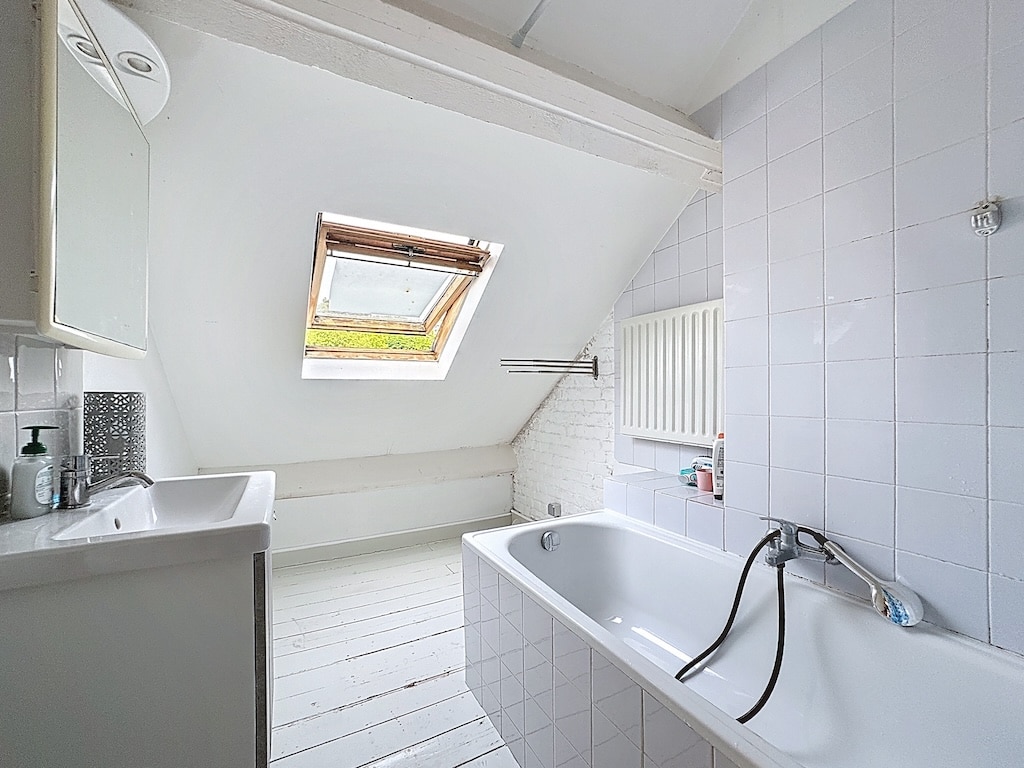 Salle de bain attic lumineuse, moderne, avec baignoire, douche, lavabo et lumière naturelle.
