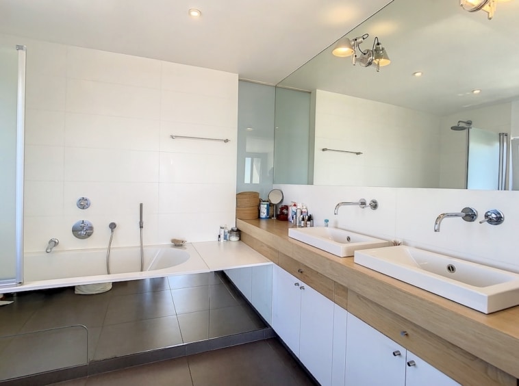 Salle de bain contemporaine avec double lavabo, baignoire et douche en design minimaliste blanc et bois.