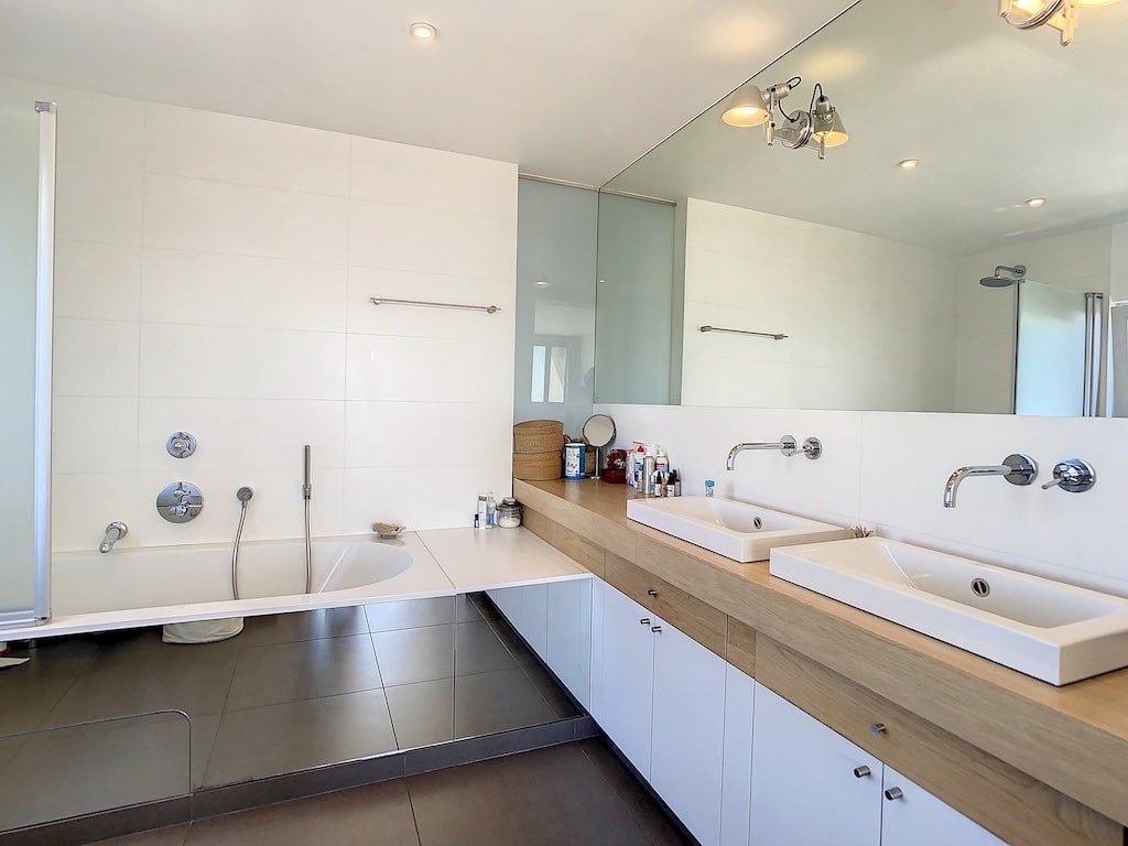 Salle de bain contemporaine avec double lavabo, baignoire et douche en design minimaliste blanc et bois.