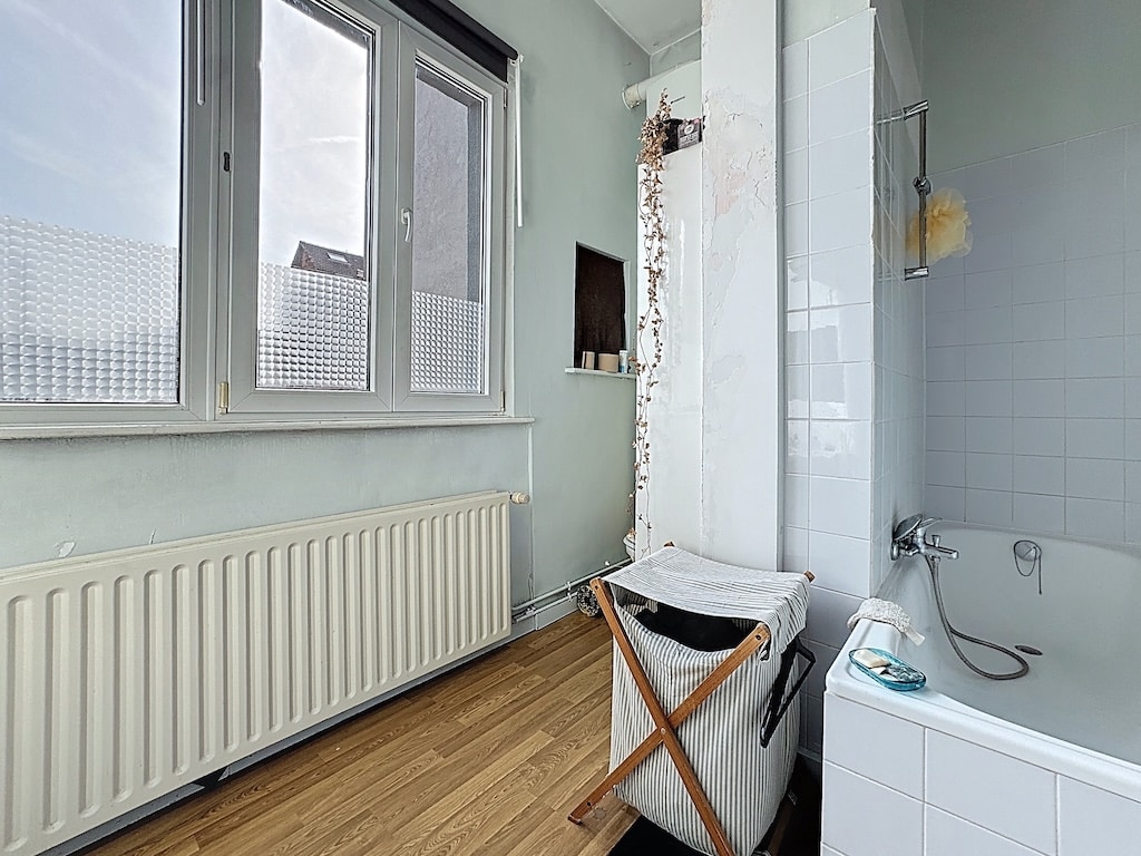 Salle de bain lumineuse avec baignoire blanche, fenêtres, plancher en bois et rangement pratique.