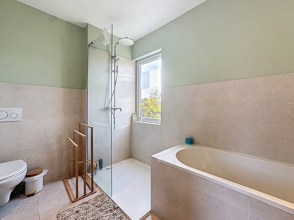 Salle de bain moderne avec douche en verre, baignoire blanche et touches naturelles en bois.
