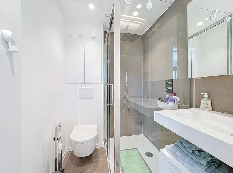 Salle de bain moderne, épurée, douche à l’italienne, WC suspendu, rangement élégant, ambiance neutre.