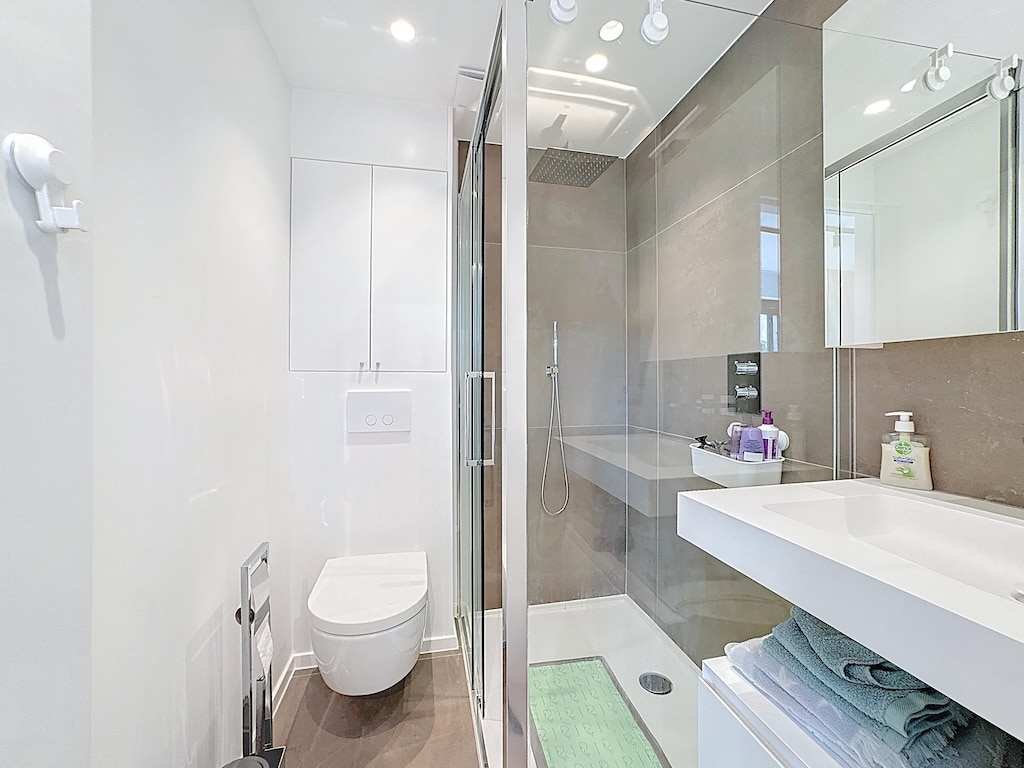 Salle de bain moderne, épurée, douche à l’italienne, WC suspendu, rangement élégant, ambiance neutre.