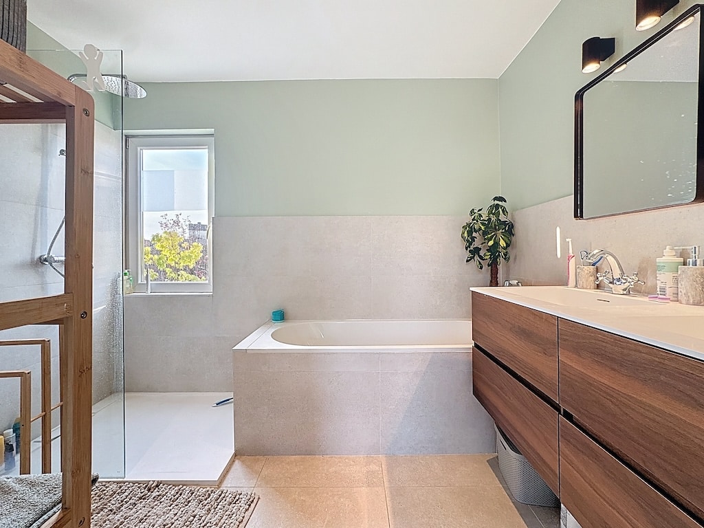 Salle de bain moderne, lumineuse et zen avec douche en verre, baignoire élégante et touches de nature.