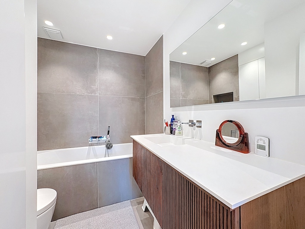 Salle de bain moderne et lumineuse avec vanity en bois, baignoire minimaliste et éclairage intégré.
