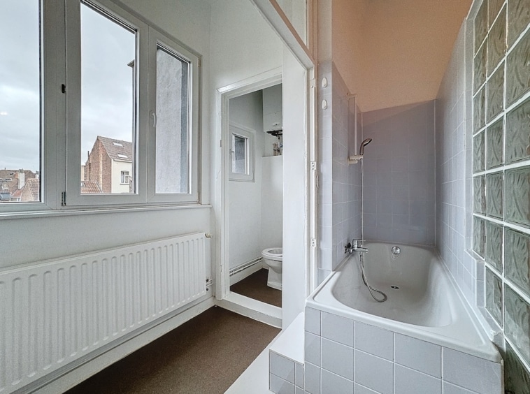 Salle de bain moderne lumineuse avec vue urbaine, baignoire blanche et douche en verre élégante.