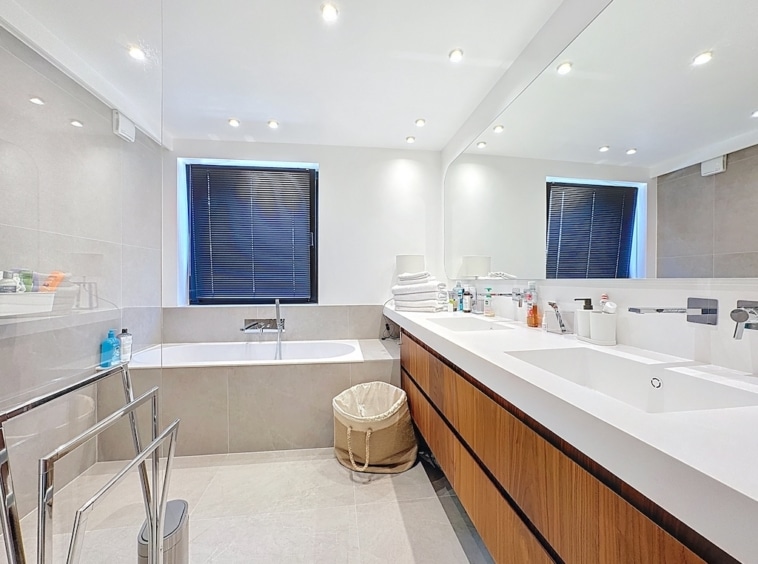Salle de bains moderne avec baignoire, double lavabo, lumière naturelle et finition élégante.