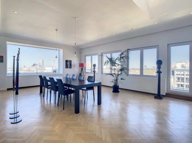 Salle de réunion moderne avec vue urbaine, grande table en bois, lumière naturelle et décoration élégante.