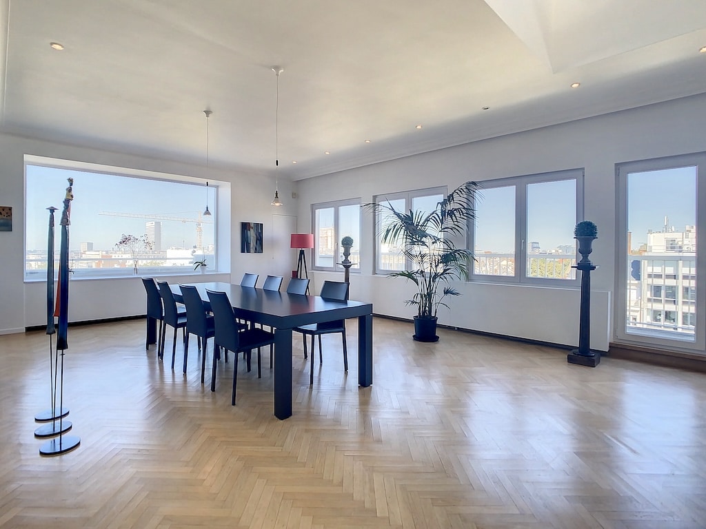Salle de réunion moderne avec vue urbaine, grande table en bois, lumière naturelle et décoration élégante.