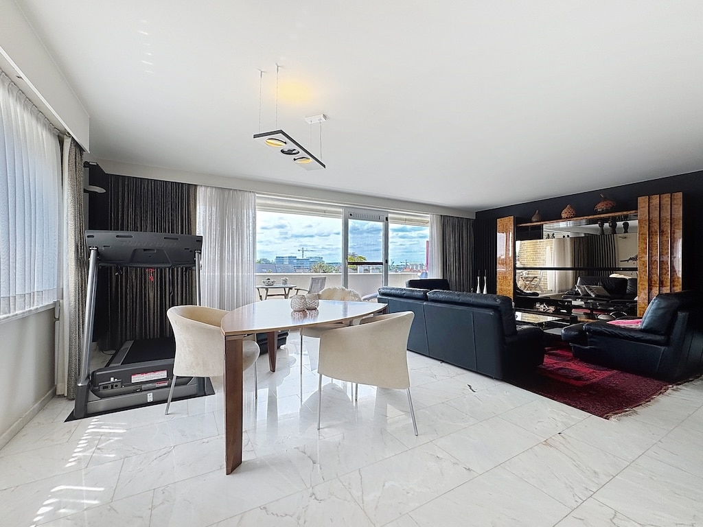 Salon moderne lumineux avec coin repas, canapé noir, tapis rouge et espace fitness.