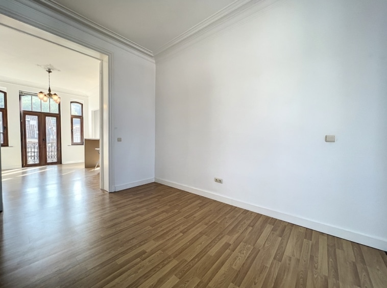 Espace lumineux et minimaliste avec sol en bois, murs blancs et grandes fenêtres intégrant la lumière naturelle.