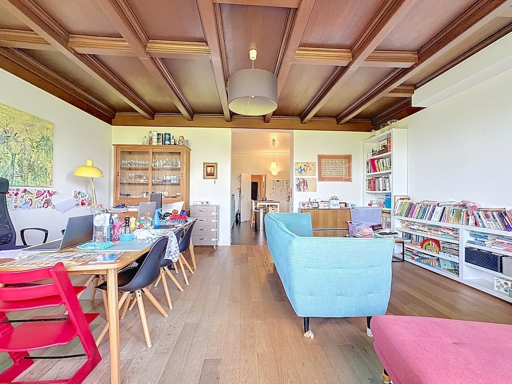 Salon chaleureux avec canapé bleu, fauteuil rose, table à manger rouge, bibliothèque et décor accueillant.