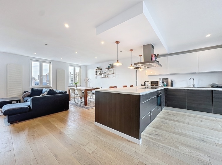 Salon et cuisine modernes, espace lumineux avec îlot blanc, canapé bleu foncé, vue panoramique.