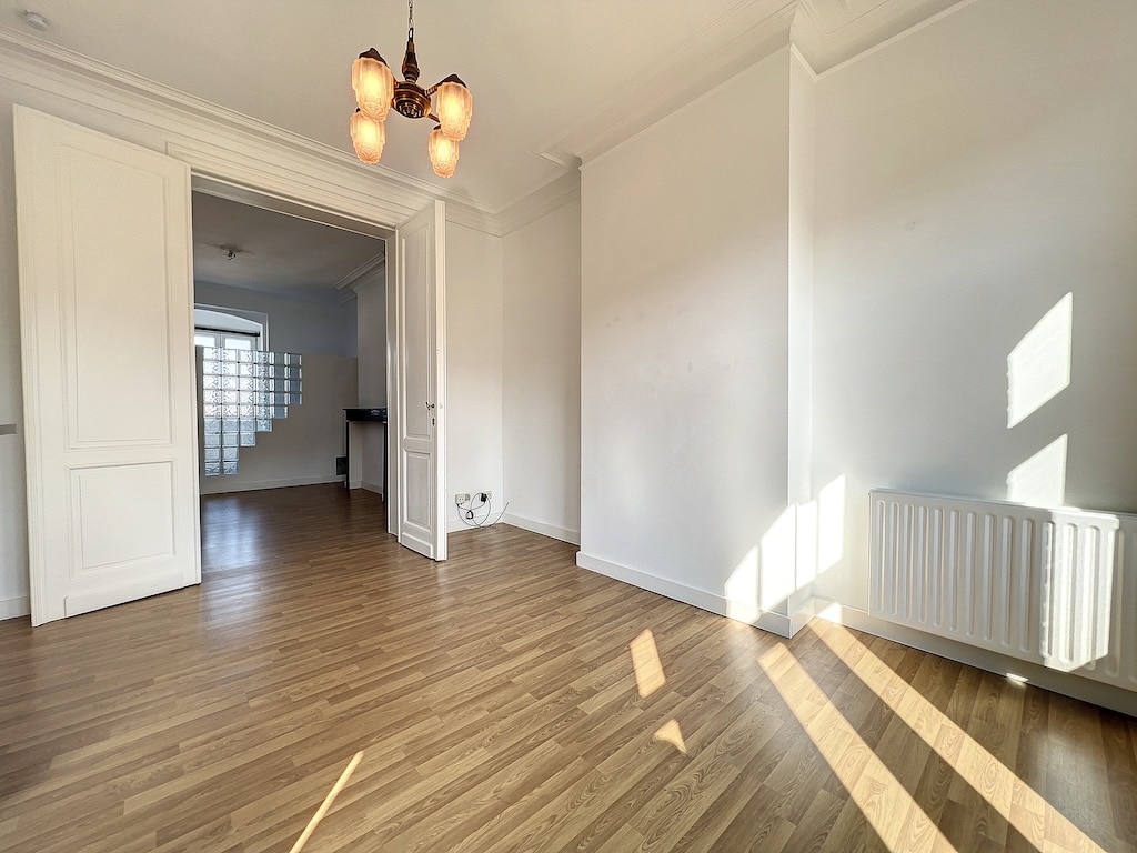 Salon lumineux avec grande fenêtre, bois clair, éclairage élégant, ambiance chaleureuse et accueillante.