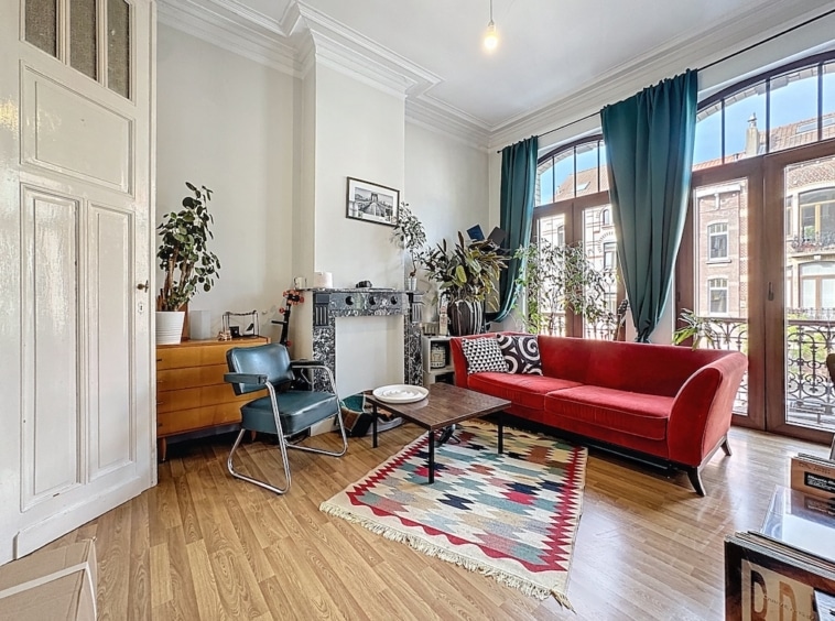 Salon moderne avec canapé rouge, plantes, grandes fenêtres et décor élégant.