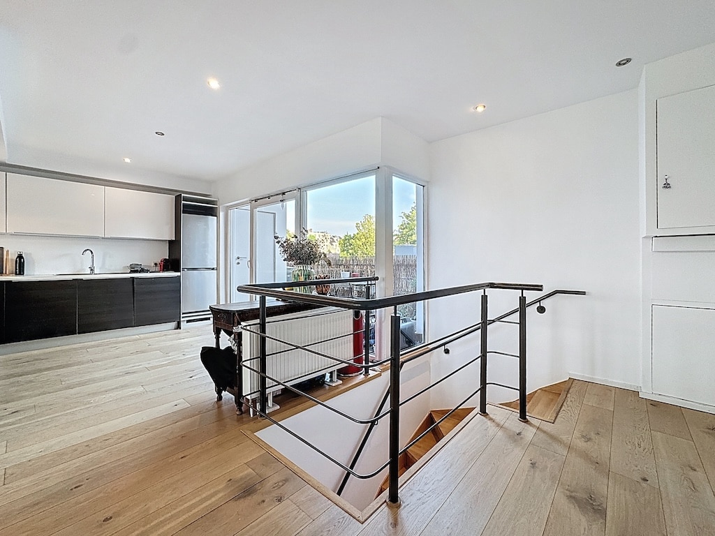 Salon contemporain lumineux avec cuisine moderne, escalier en métal noir, vue sur jardin verdoyant.