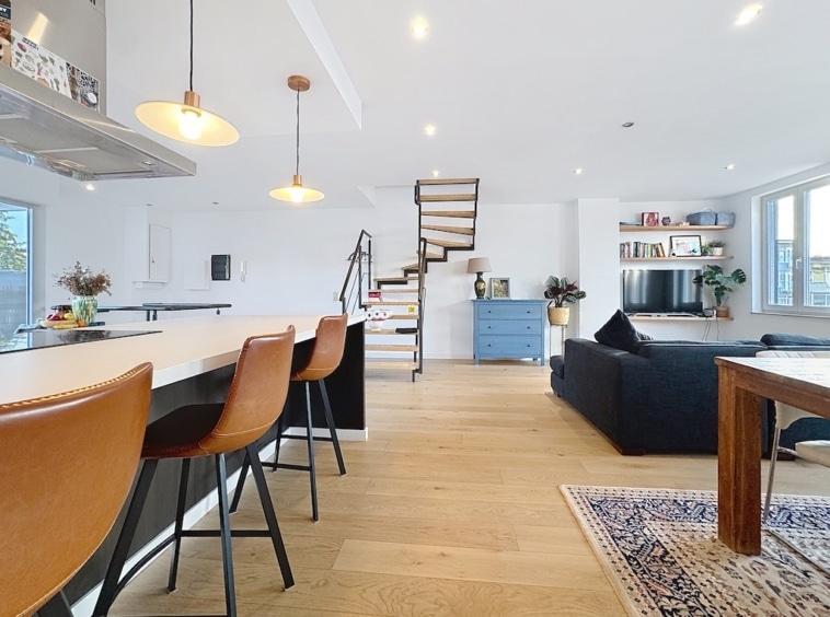 Salon contemporain avec cuisine ouverte, escalier spiralé, mobilier moderne et décoration élégante.