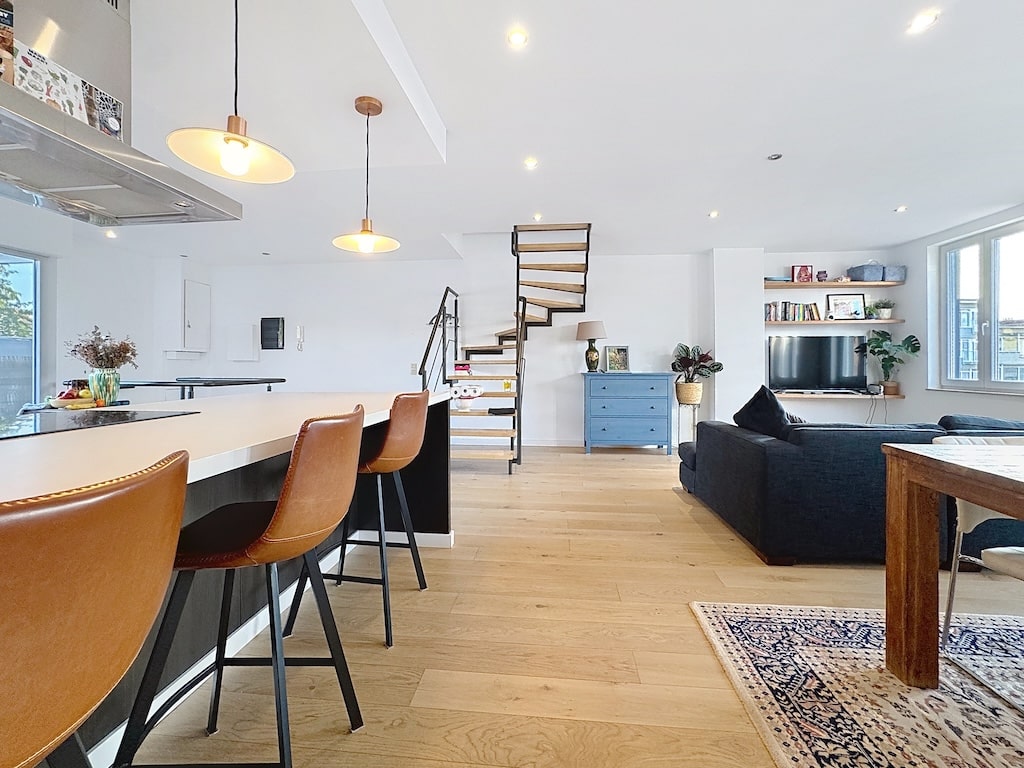 Salon contemporain avec cuisine ouverte, escalier spiralé, mobilier moderne et décoration élégante.