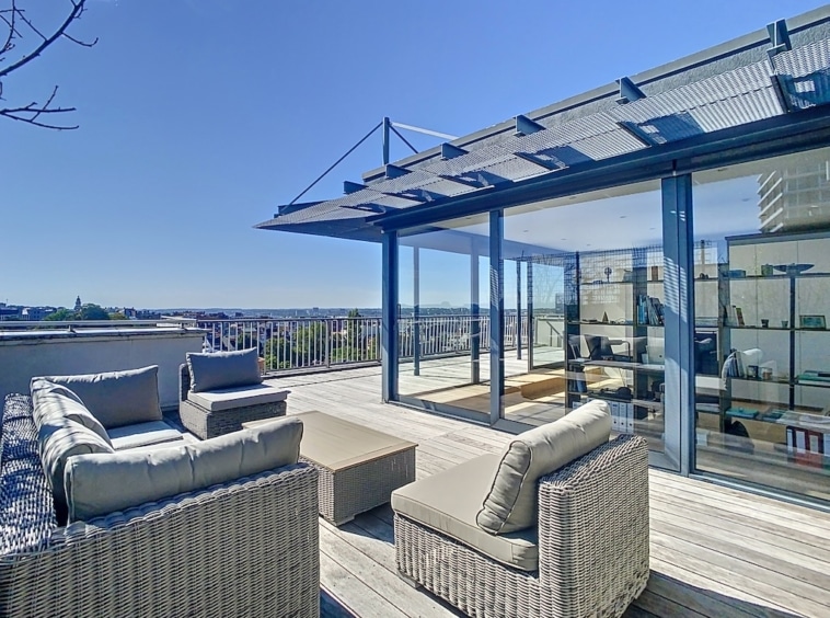 Terrasse moderne en bois avec vue urbaine, mobilier en osier, ambiance élégante et détente assurée.