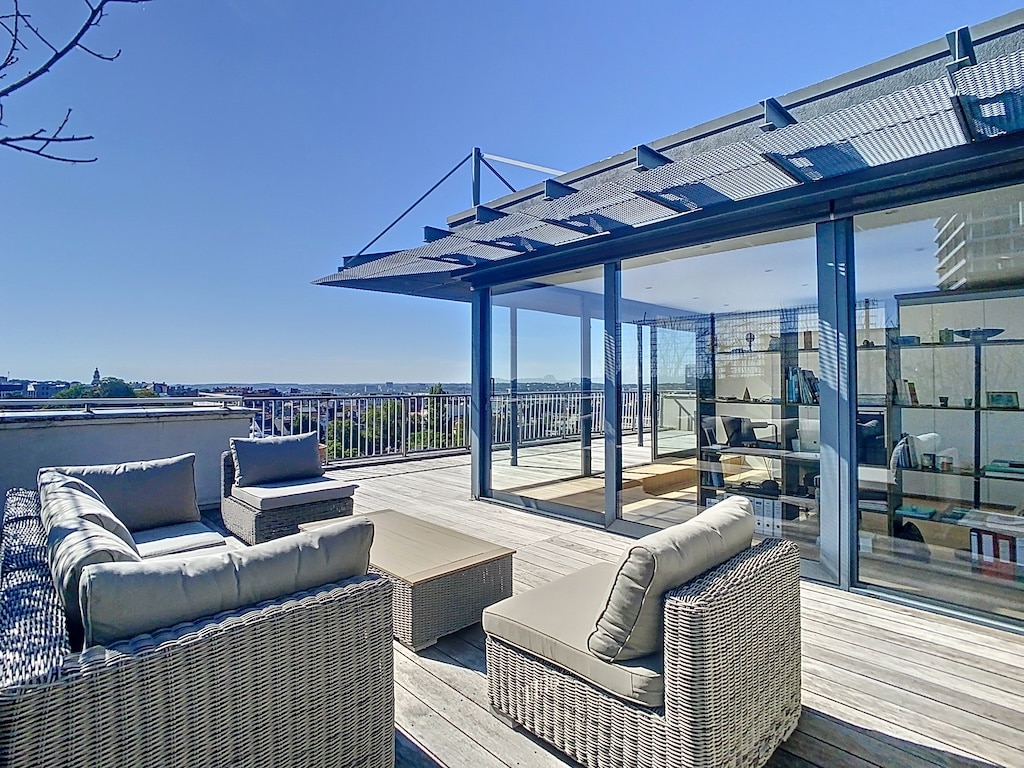 Terrasse moderne en bois avec vue urbaine, mobilier en osier, ambiance élégante et détente assurée.