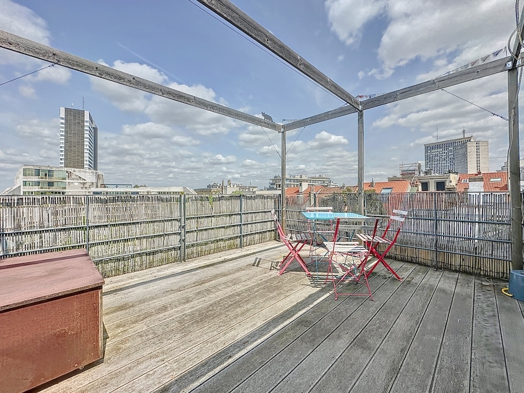 Terrasse urbaine en bois avec mobilier coloré, vue sur la ville et ambiance détendue.