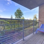 Balcon minimaliste avec fauteuil bleu, vue verdoyante, ambiance paisible et design contemporain.
