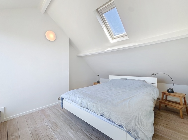 Chambre attic lumineuse minimaliste avec lit moderne, plancher en bois clair et lumière naturelle.
