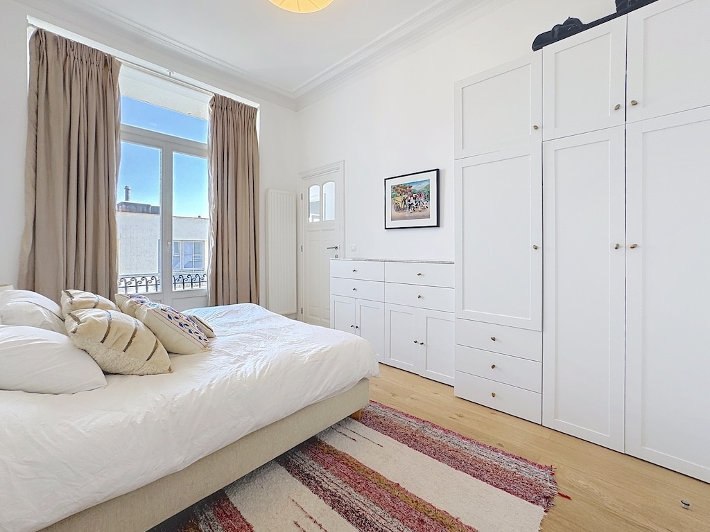 Chambre lumineuse et minimaliste avec lit, armoire, tapis coloré et vue naturelle apaisante.