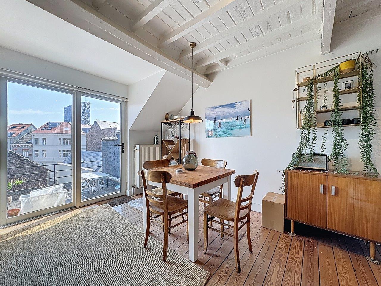 Espace repas lumineux avec mobilier en bois, vue sur toits et décoration végétale chaleureuse.