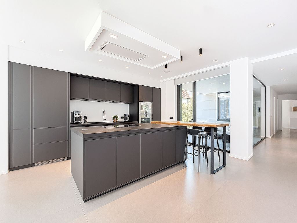 Cuisine moderne minimaliste avec îlot sombre, éclairage chaleureux et grande baie vitrée, style contemporain.